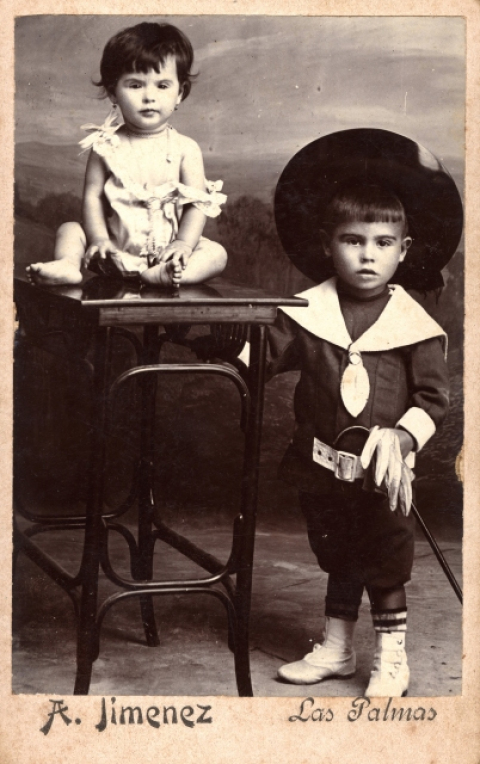 RETRATO DE NIÑA SOBRE MESA, CON NIÑO DISFRAZADO DE MOSQUETERO DE PIE A SU LADO